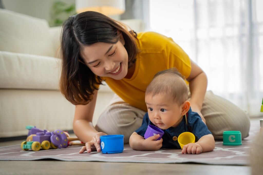 A woman is playing with a baby on the floor. The baby is holding a blue and purple toy