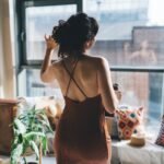 Anonymous woman in dress standing near window at home