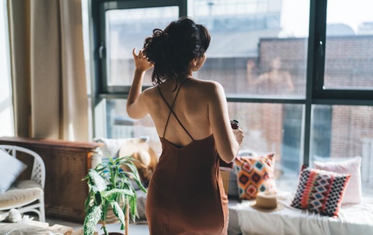 Anonymous woman in dress standing near window at home