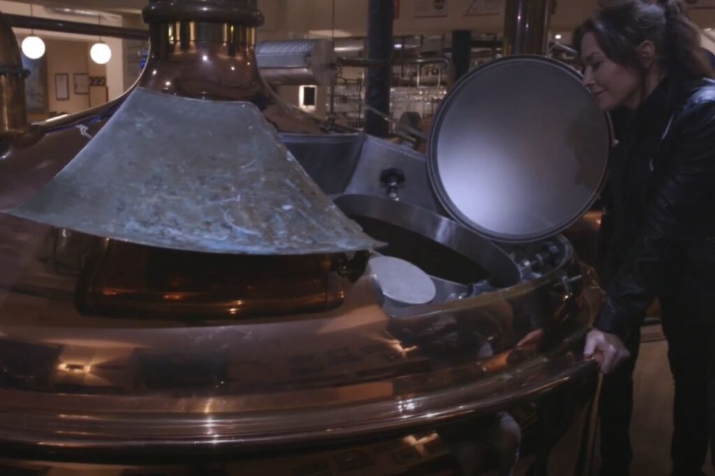 A woman examines a large copper brewing vat inside Brauhaus Dessau, observing the beer-making process up close in the brewery.