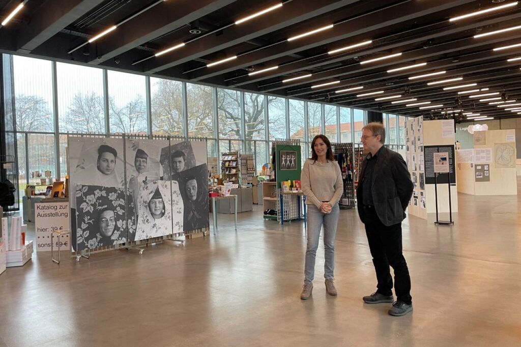 A woman and a man stand in front of a large black-and-white photo collage inside the Bauhaus Museum gift shop and exhibit area in Dessau.