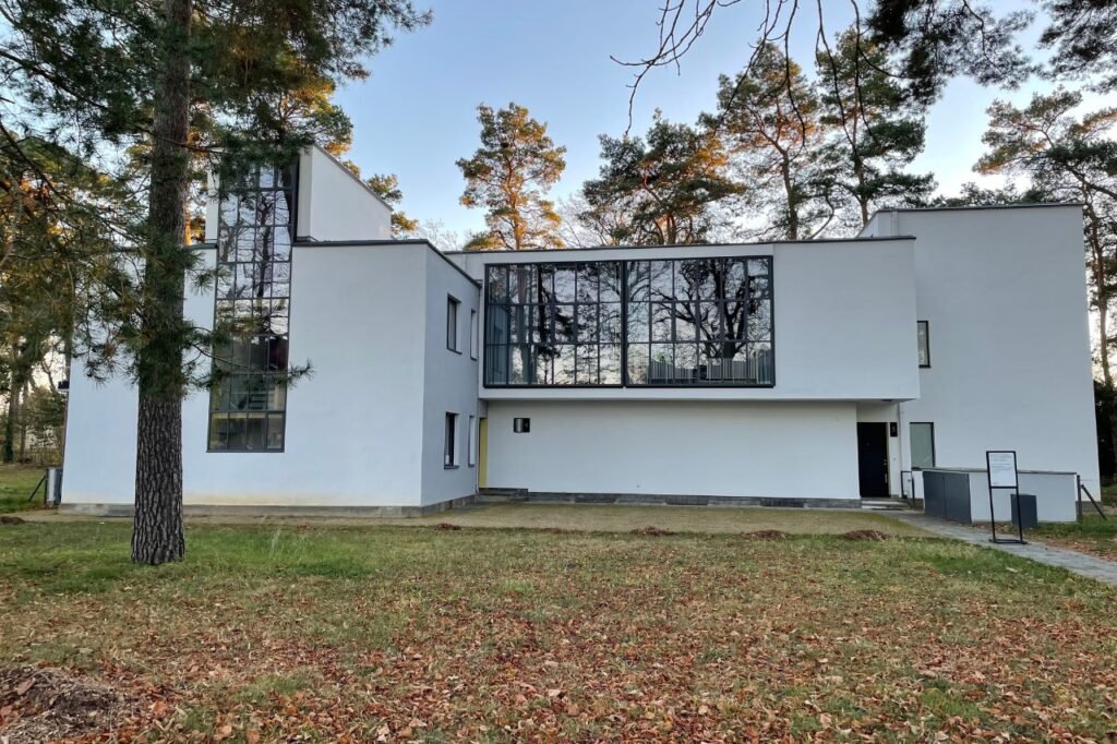 Exterior view of a Masters’ House in Dessau, Germany—featuring clean lines, geometric shapes, and large glass windows surrounded by trees.
