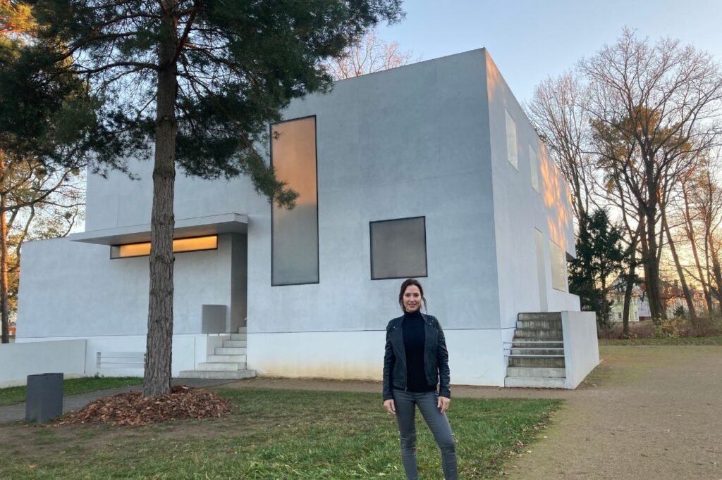 A woman stands in front of a minimalist white Bauhaus-style house with rectangular windows and sharp edges in the Masters' Houses complex in Dessau.
