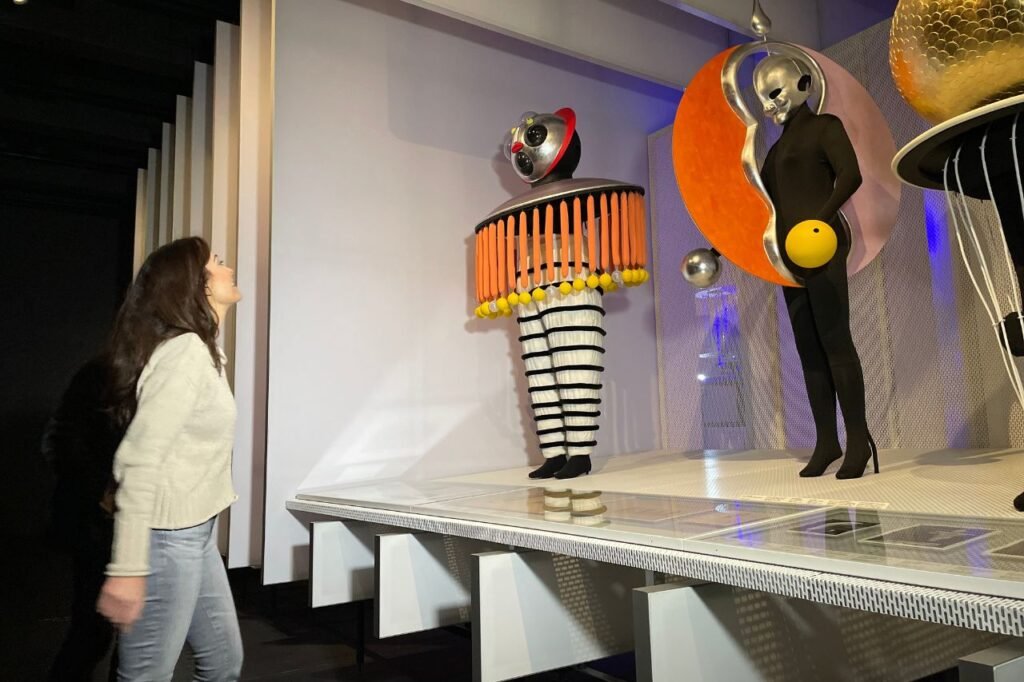 A woman observes colorful, avant-garde Bauhaus stage costumes on display at the Bauhaus Museum Dessau, showcasing the movement’s theatrical design legacy.
