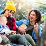 Happy family camping in the forest playing guitar and singing together