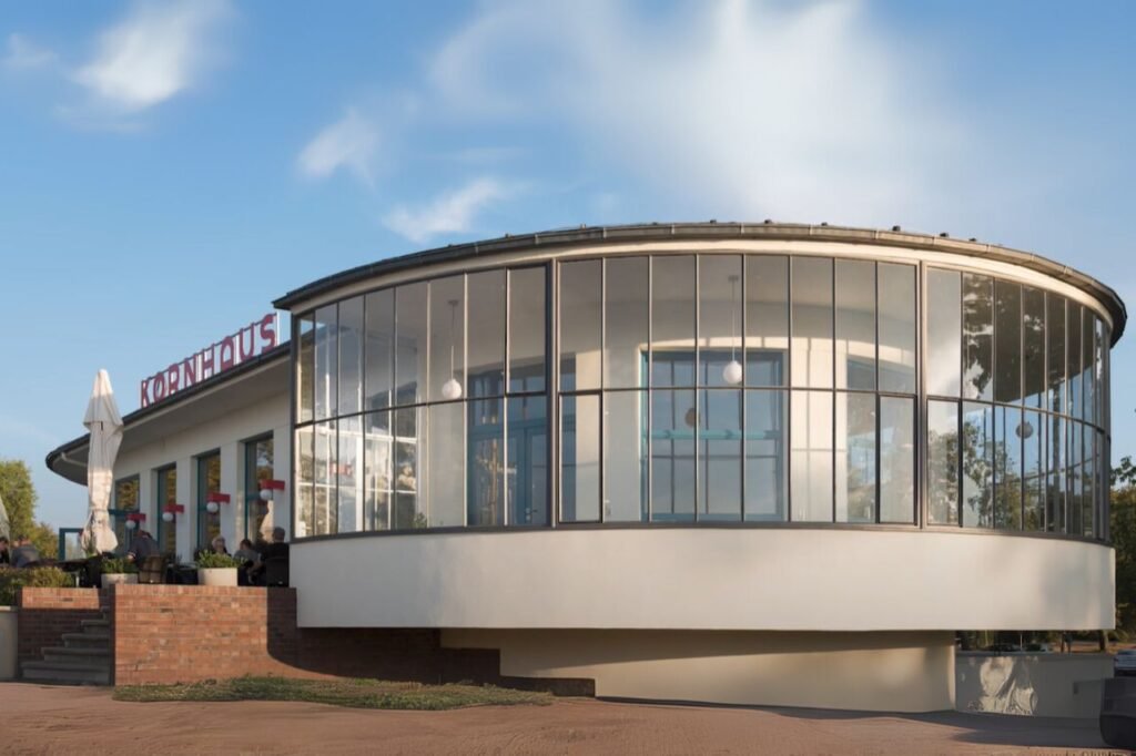 Exterior view of the Kornhaus Restaurant in Dessau, a curved glass Bauhaus building designed by Carl Fieger, overlooking the Elbe River.