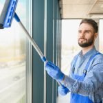 Young man cleaning window in office