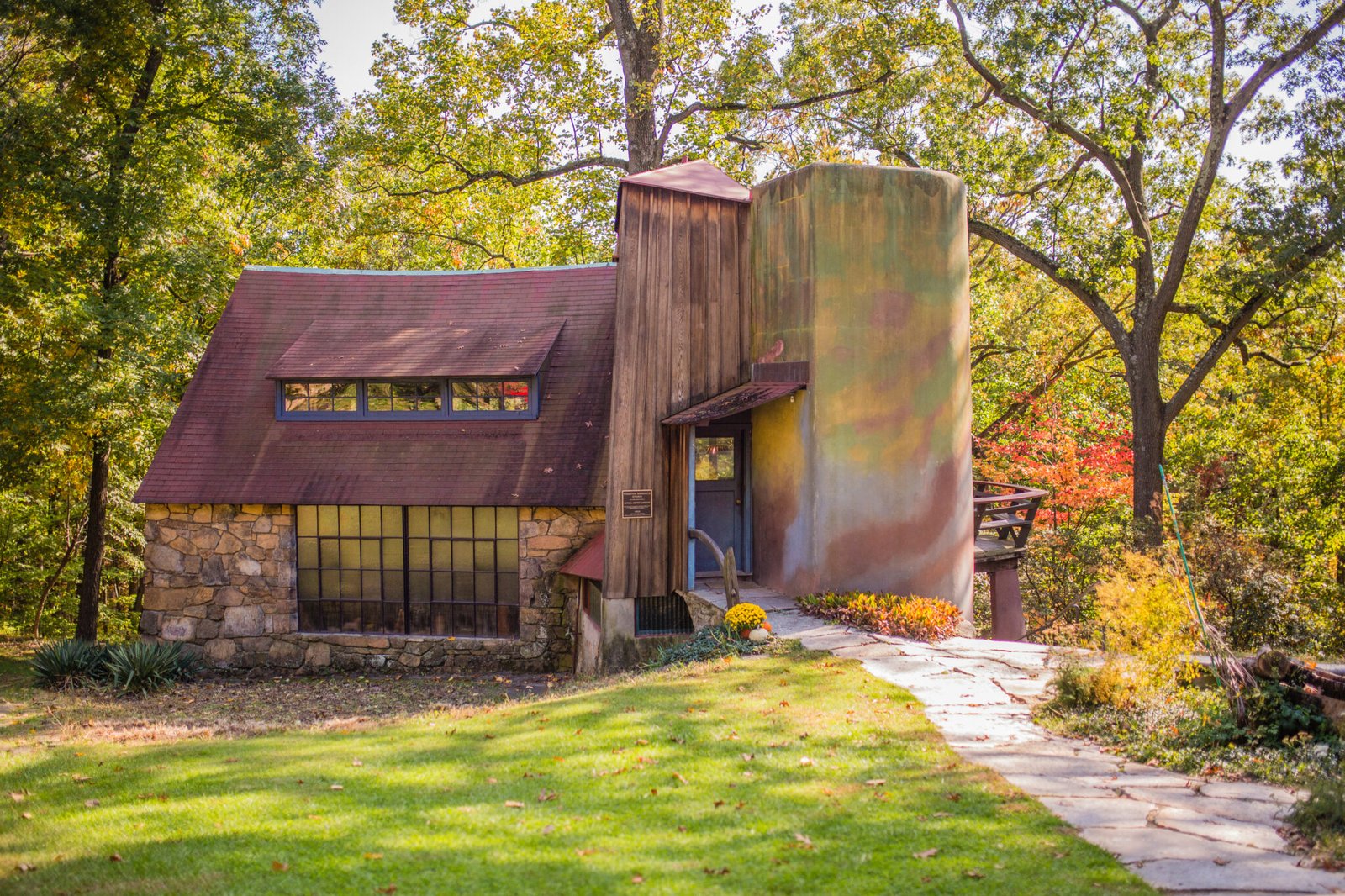 Exterior of the Wharton Esherick Museum studio in Malvern, Pennsylvania, featuring a rustic stone base, sloped red roof, and cylindrical tower surrounded by trees.