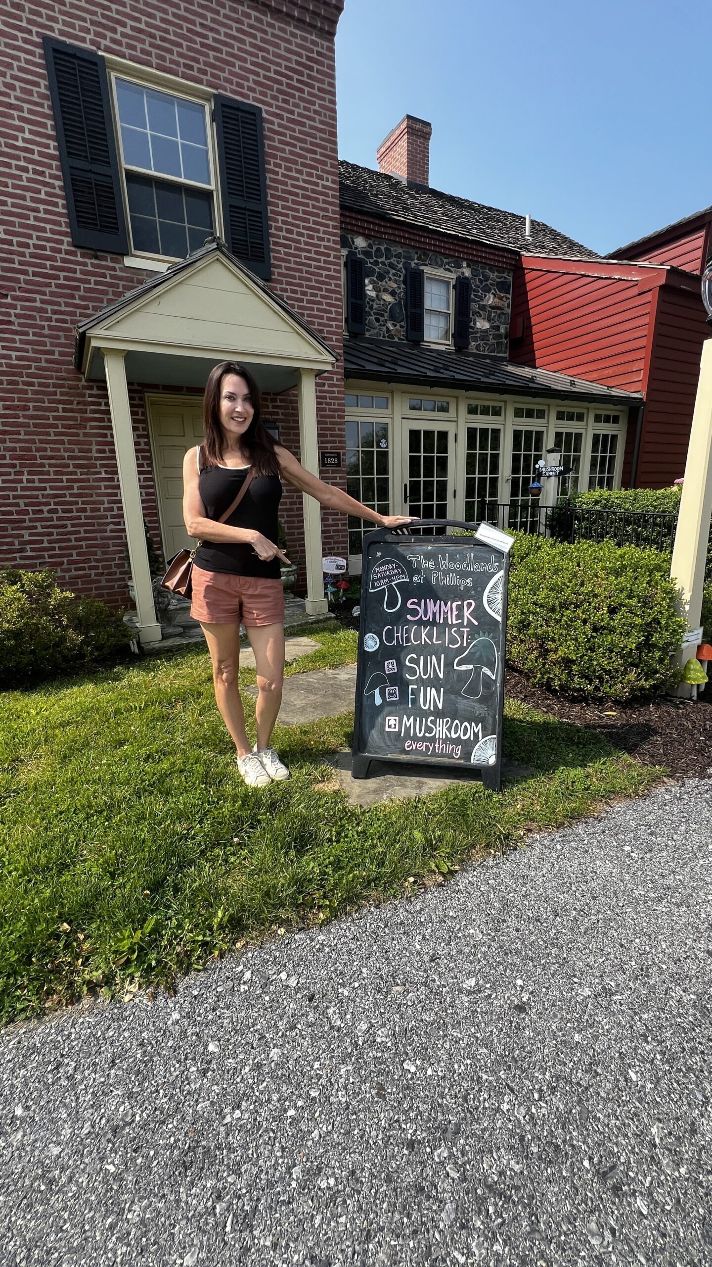 Kennett Square: Exploring the Mushroom Capital of the World Woman standing outside a farmhouse pointing to a chalkboard sign that reads “Summer Checklist: Sun, Fun, Mushroom Everything.”