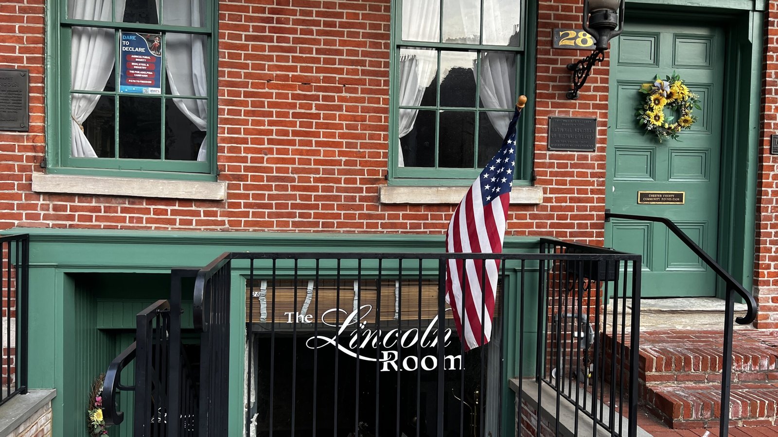 Close-up of The Lincoln Room entrance with American flag, green door, and brick exterior.