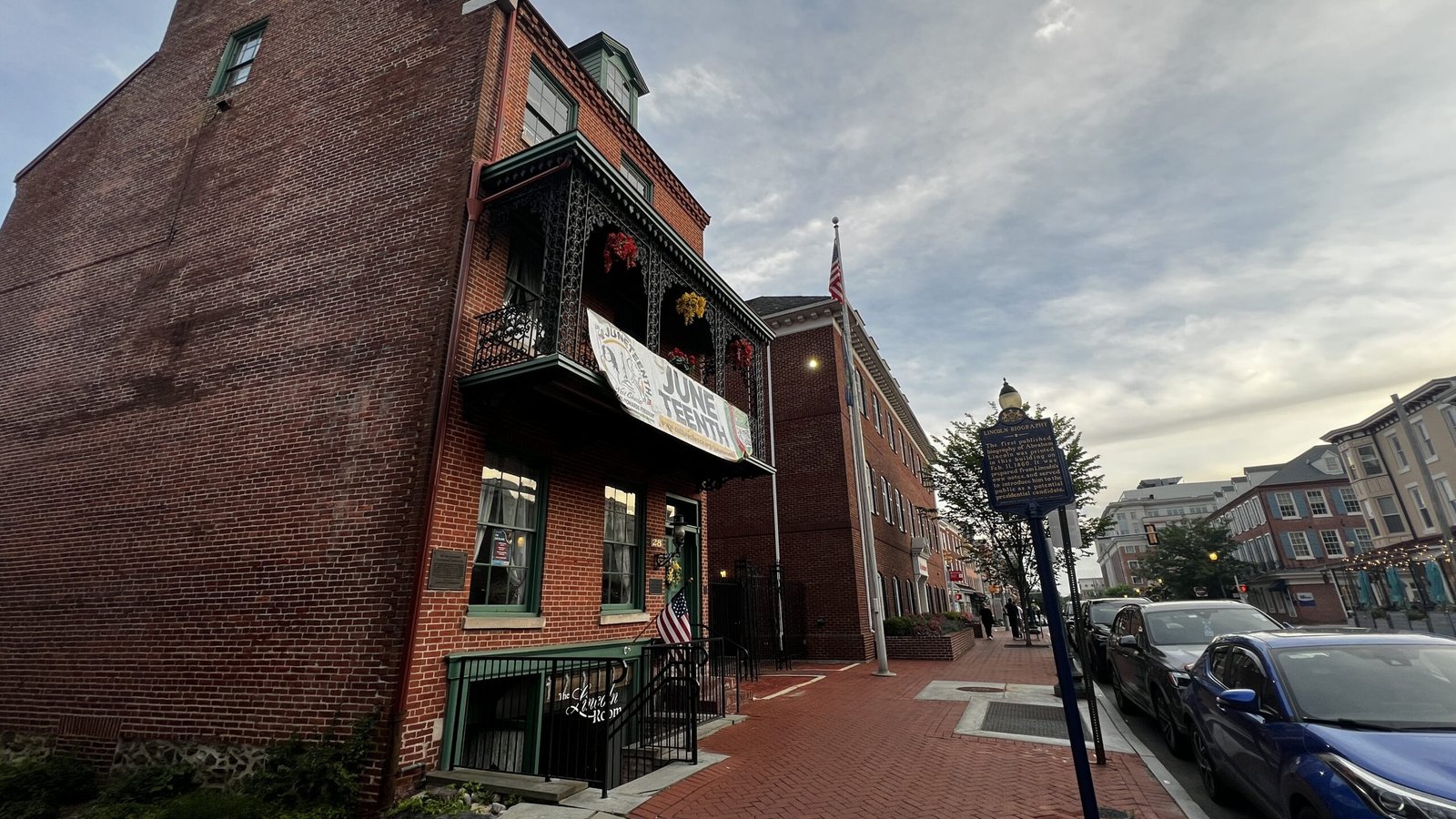Brick building in West Chester with historic markers and June teenth banner on the balcony.
