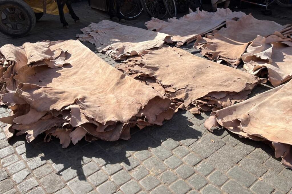 Stacks of raw, untreated leather hides laid out on cobblestone ground at a Marrakech tannery in Morocco.