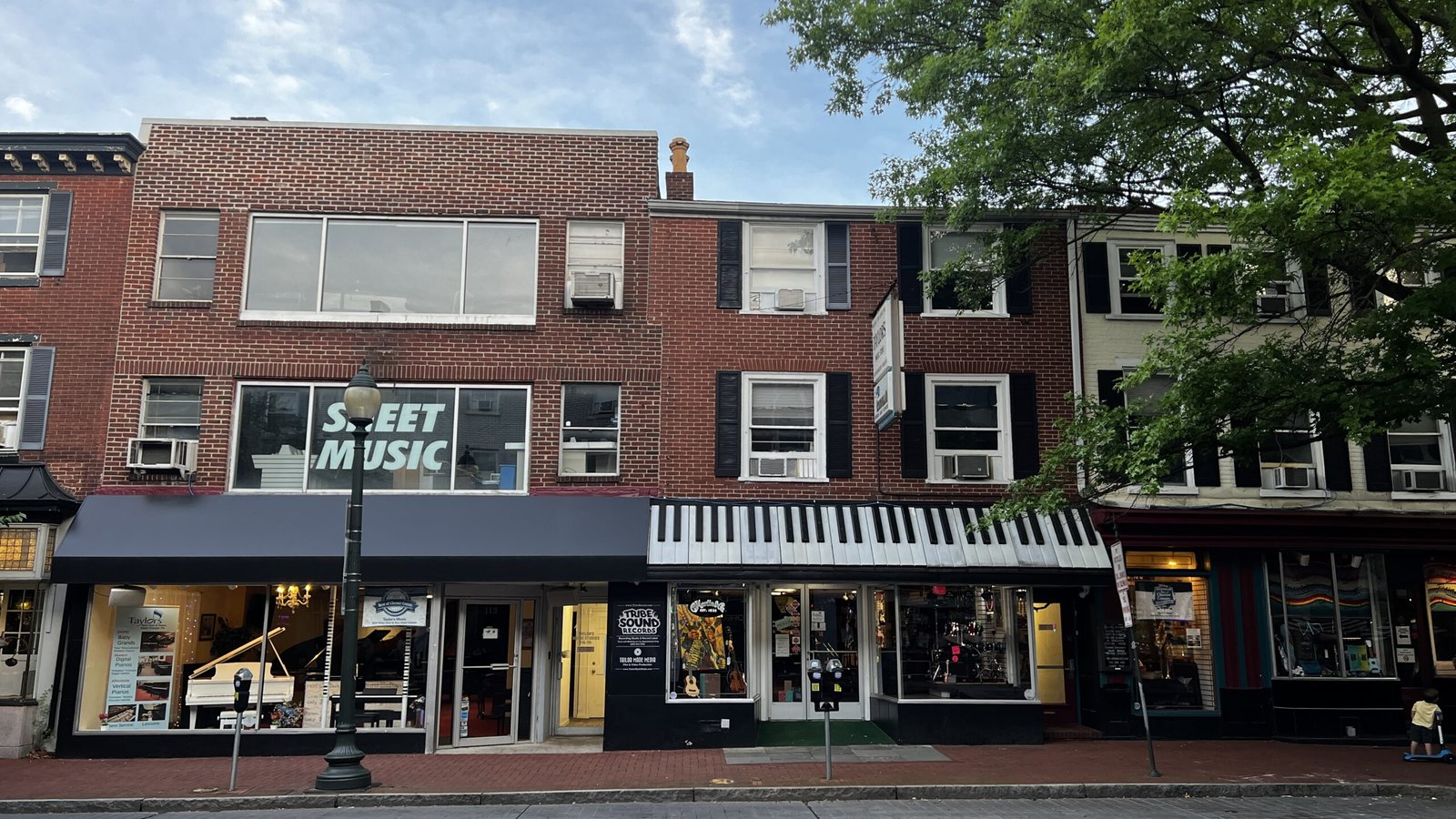 Row of brick storefronts on Main Street in West Chester with shops, display windows, and a piano-themed awning.