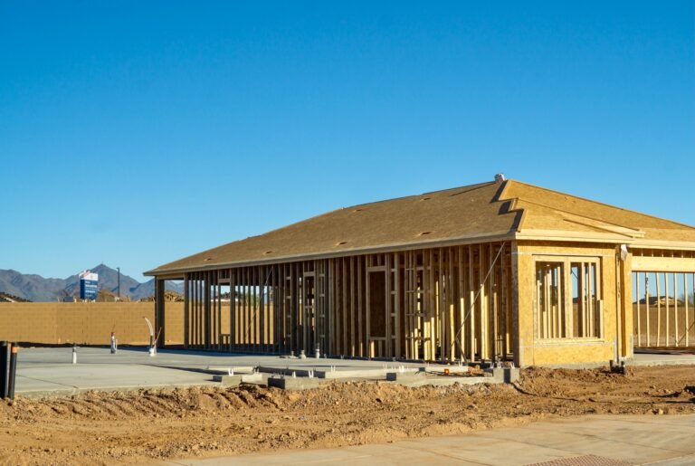 A framed house under construction and a concrete slab foundation with plumbing ready for framing