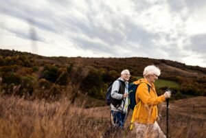 Active senior couple with backpacks hiking together in nature on autumn day.