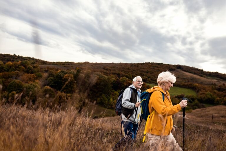 Active senior couple with backpacks hiking together in nature on autumn day.
