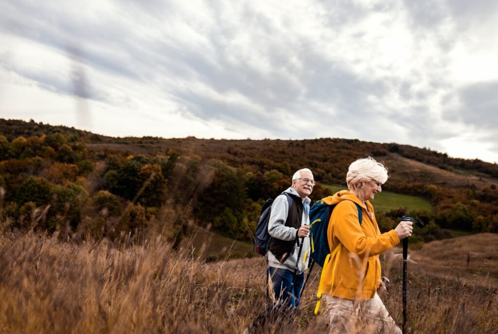 Active senior couple with backpacks hiking together in nature on autumn day.