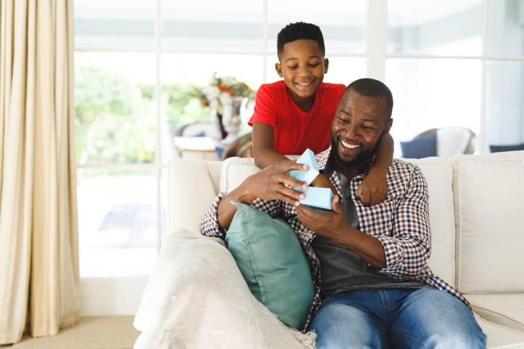 African american father opening gift from his son and smiling in living room