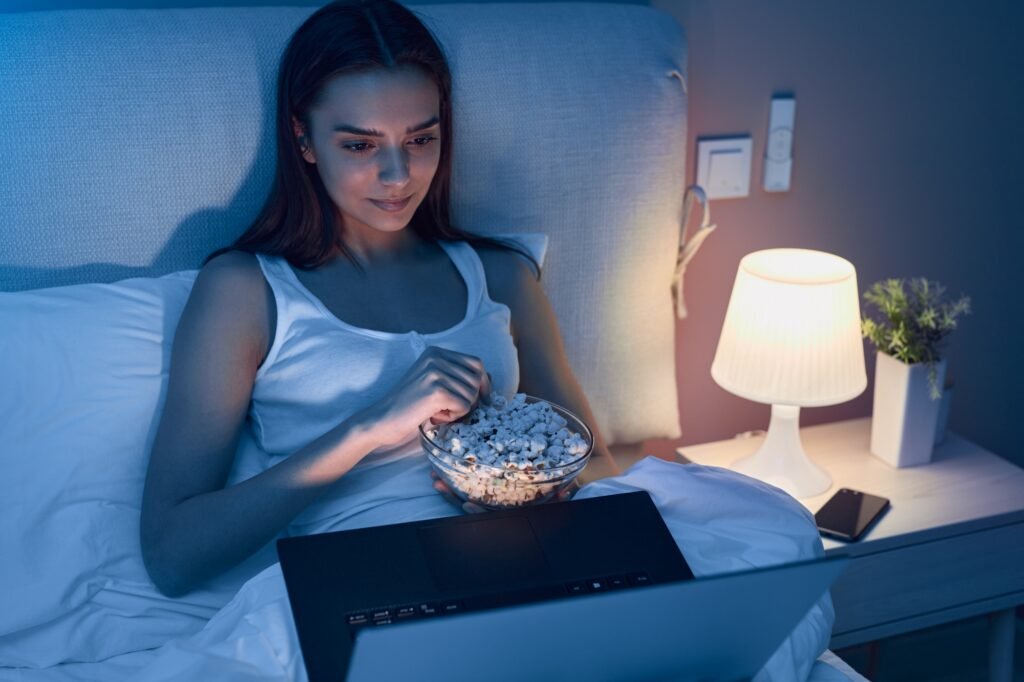Female with popcorn watching move on bed