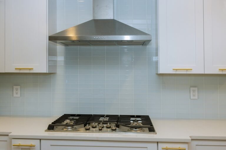 Kitchen features white cabinets with marble countertops paired with stone stainless steel hood