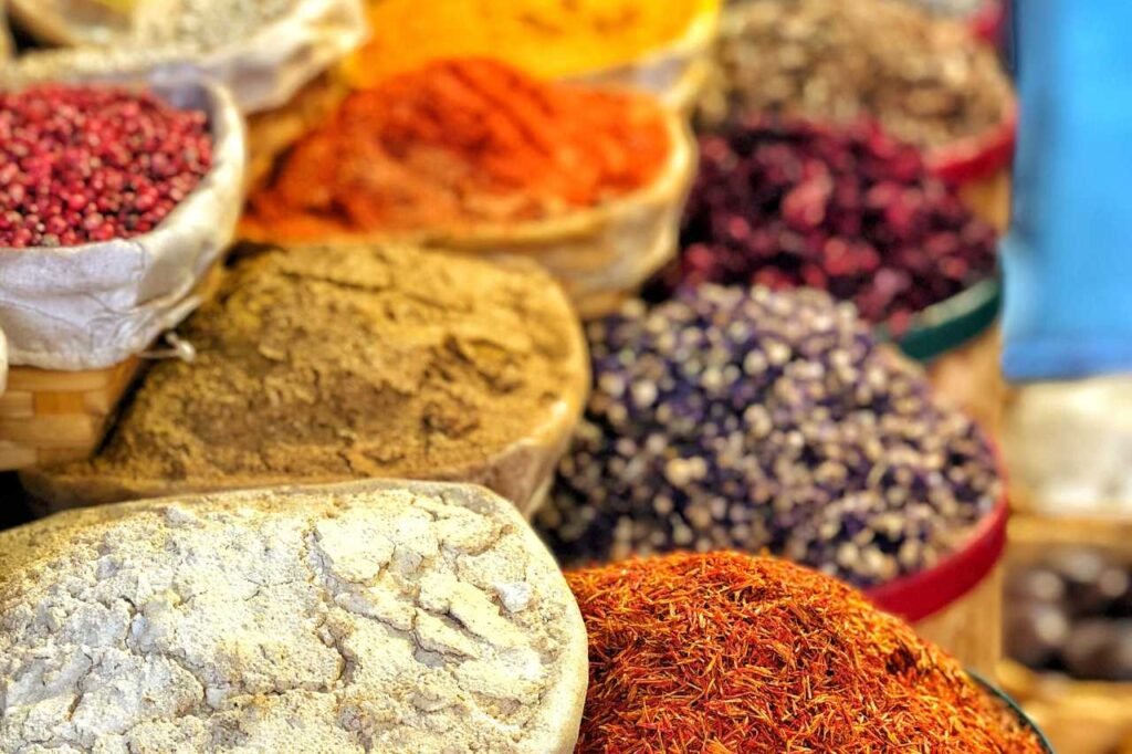 Colorful baskets of spices, including saffron, cumin, and turmeric, displayed in the narrow lanes of Hay Elmellah, the old Jewish Quarter, their vibrant hues standing out against the historic backdrop.