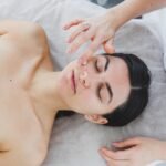 The face of a young woman to whom a beautician applies cream to her skin. Facial. Facial skin care