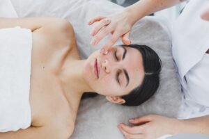 The face of a young woman to whom a beautician applies cream to her skin. Facial. Facial skin care