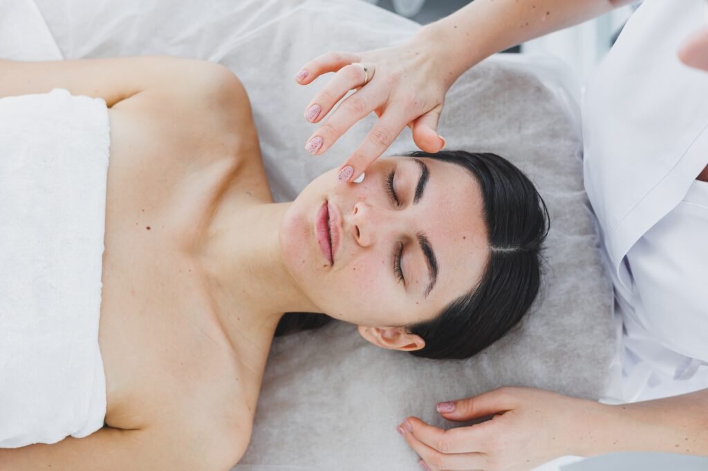 The face of a young woman to whom a beautician applies cream to her skin. Facial. Facial skin care