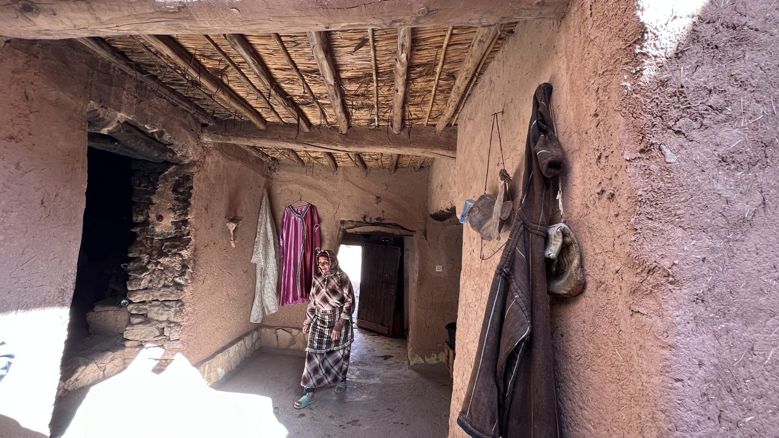 Local woman walking inside a traditional mudbrick passageway in Aït Benhaddou with wooden ceiling beams.