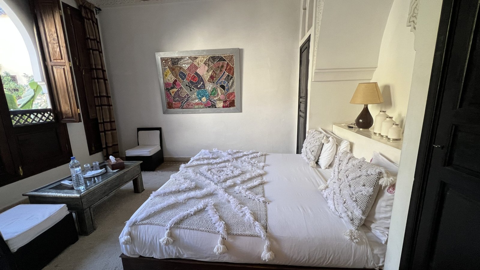 Guestroom at Riad Pachavana with a white bedspread, wooden window, and colorful artwork.