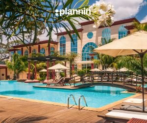 Luxury resort pool area with lounge chairs, palm trees, and a large building with arched windows on a sunny day, featuring the text “plannin” above.