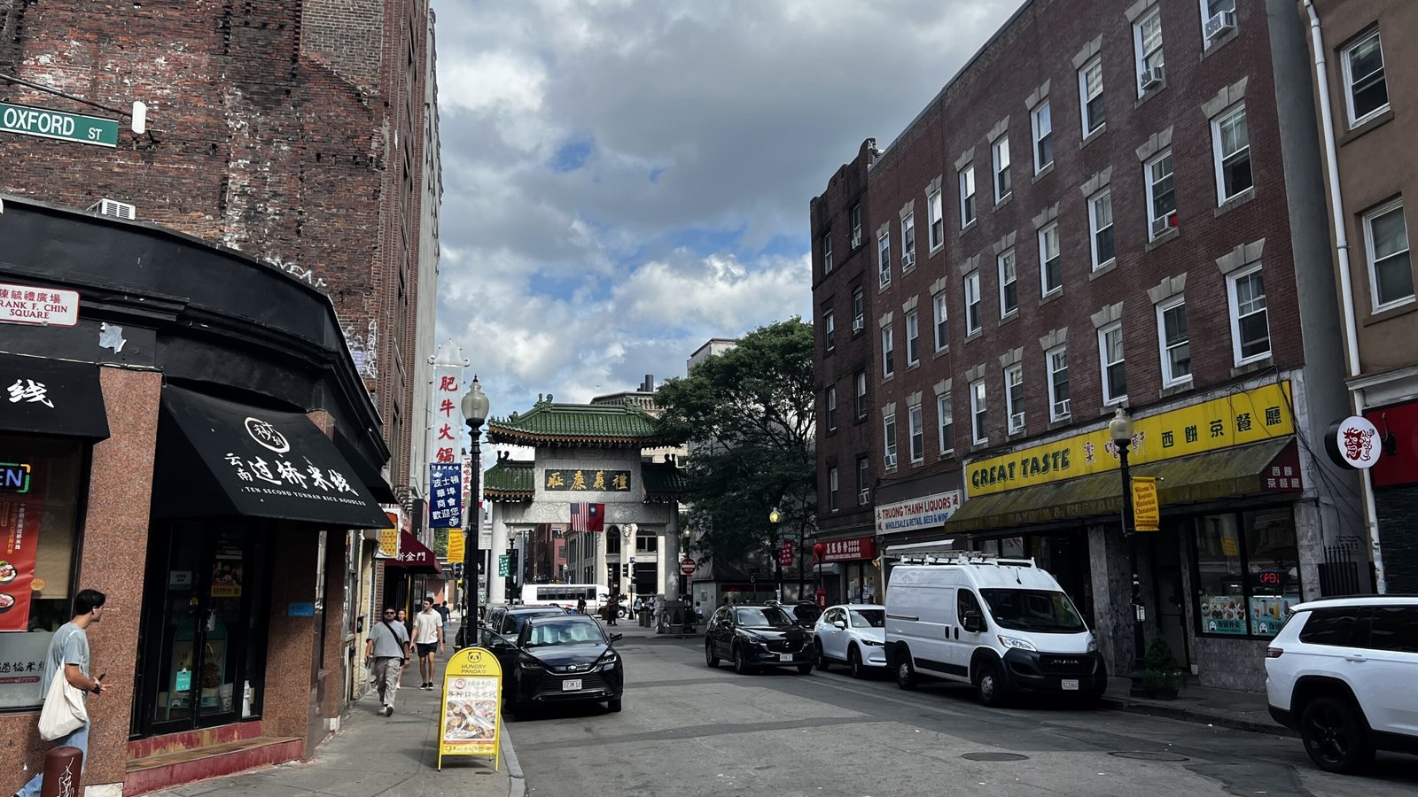 Street view of Boston’s Chinatown with restaurants, storefronts, and the Chinatown Gate visible in the distance.