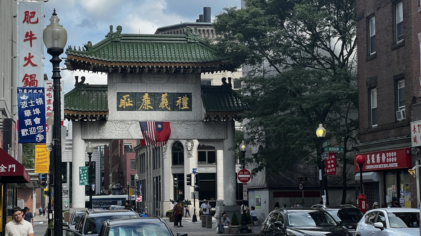 The ornate Chinatown Gate on Beach Street in Boston with Chinese inscriptions and flags displayed above the arch.