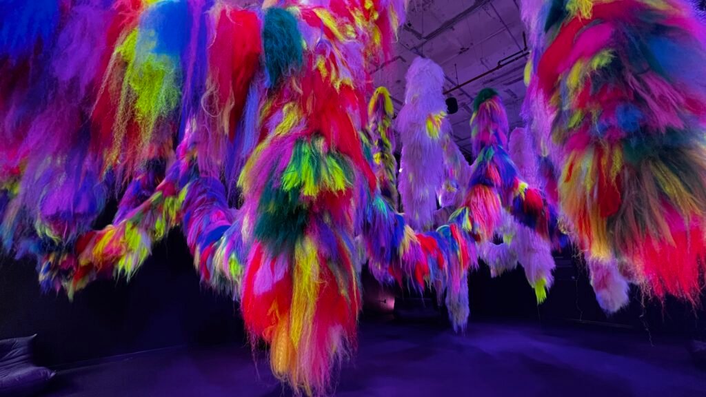 Close-up view of Shoplifter’s Nervescape installation featuring cascading strands of neon faux hair in vivid colors like red, yellow, green, and purple.