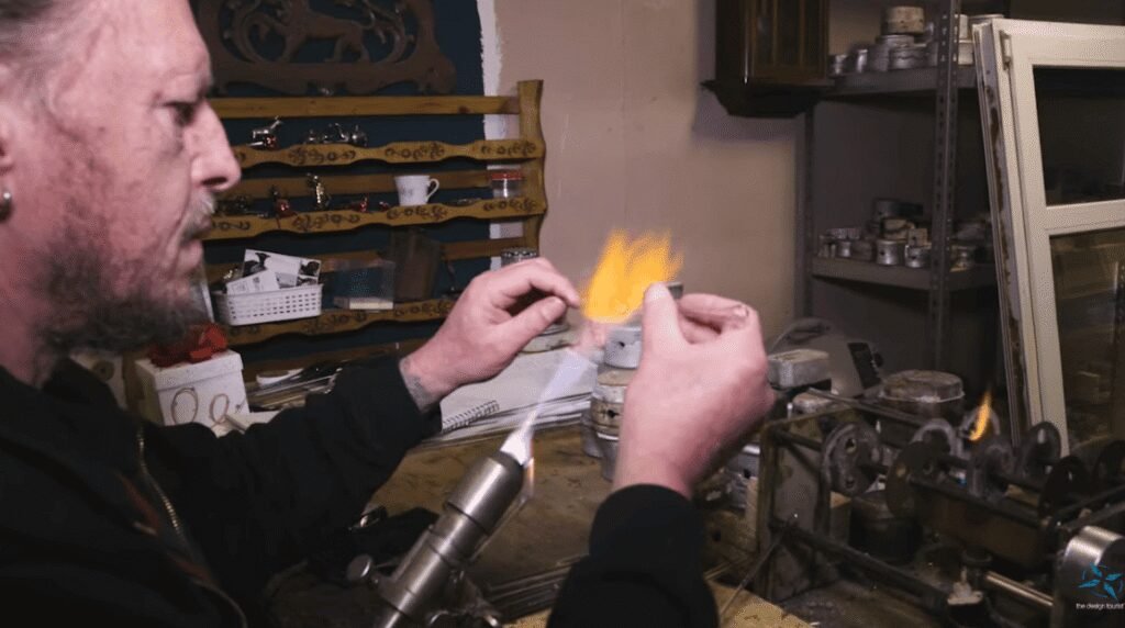 A master glassblower in Lauscha shapes molten glass over an open flame in his workshop.