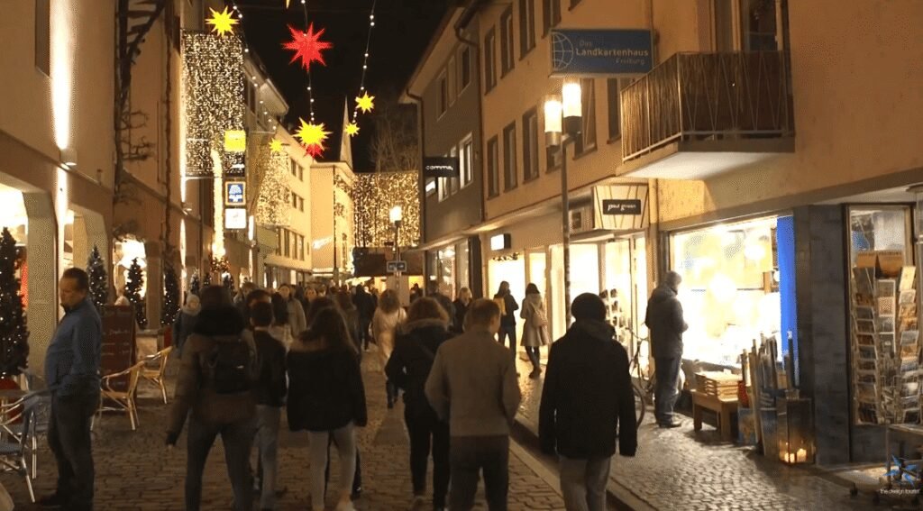 Evening crowds walk through Freiburg’s illuminated Christmas market streets decorated with stars and lights.