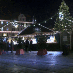Evening view of Augsburg’s Christmas market with illuminated stalls, a decorated Christmas tree, and people walking along cobblestone streets.
