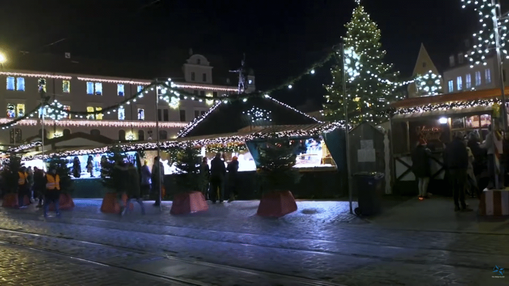 Evening view of Augsburg’s Christmas market with illuminated stalls, a decorated Christmas tree, and people walking along cobblestone streets.