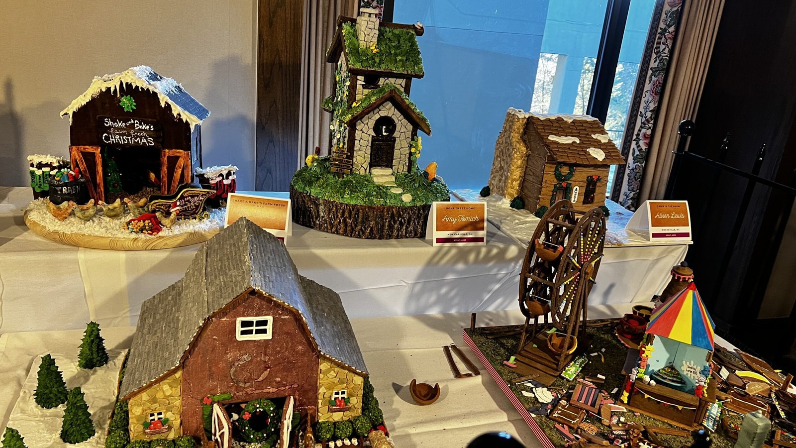 Collection of gingerbread houses inspired by cottages, barns, and village buildings displayed at the National Gingerbread House Competition inside the Omni Grove Park Inn & Spa.