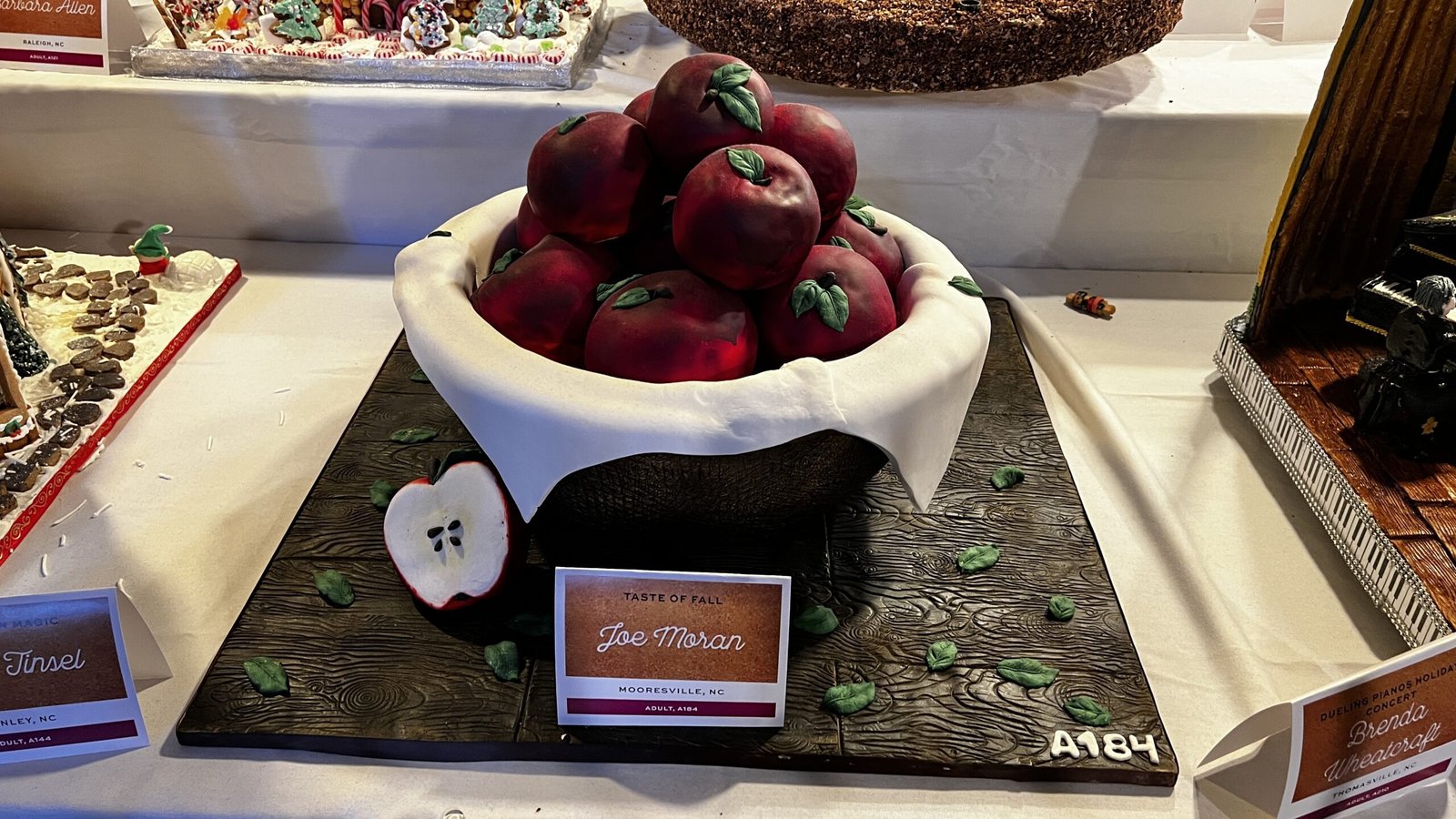 Edible gingerbread display featuring a bowl of red apples with textured leaves and a cut apple detail, shown at the National Gingerbread House Competition inside the Omni Grove Park Inn & Spa.