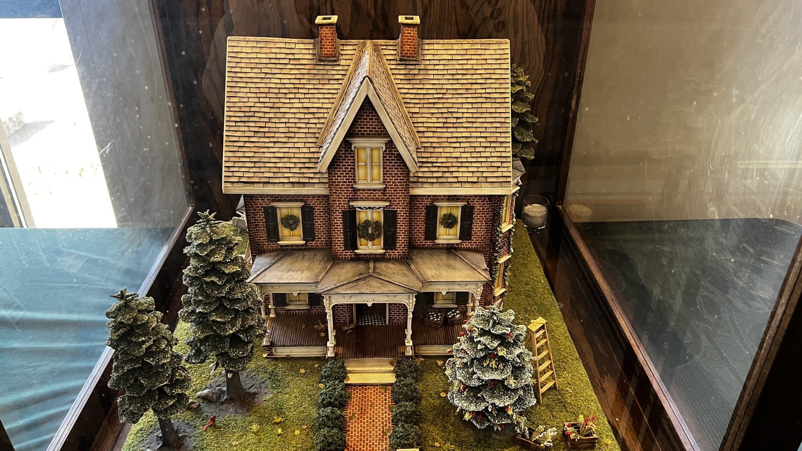Intricately crafted gingerbread house with a front porch, brick-style detailing, and landscaped trees, displayed at the National Gingerbread House Competition inside the Omni Grove Park Inn & Spa.