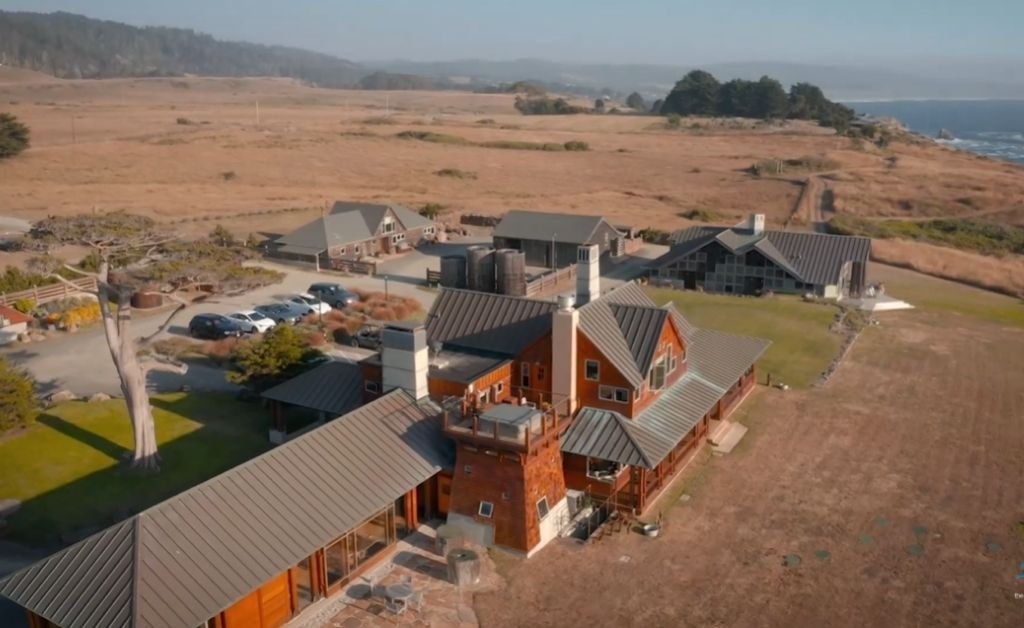 Aerial view of The Inn at Newport Ranch on the Mendocino Coast, showing the lodge buildings surrounded by open coastal meadows with the Pacific Ocean in the distance.