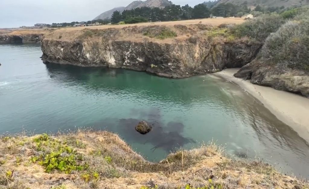 Secret Beach at The Inn at Newport Ranch, a secluded cove with clear turquoise water, sandstone cliffs and a small stretch of sandy shore.