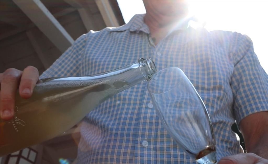 Guy pouring rustic sparkling wine into a glass at Fathers + Daughters Cellars, sunlight shining behind him.