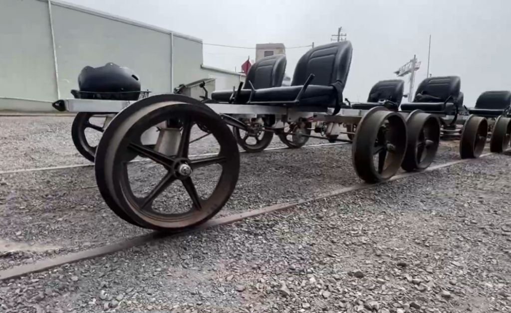 A row of open-air railbike carts with black seats and metal wheels positioned on gravel tracks, ready for a Mendocino railbike tour.