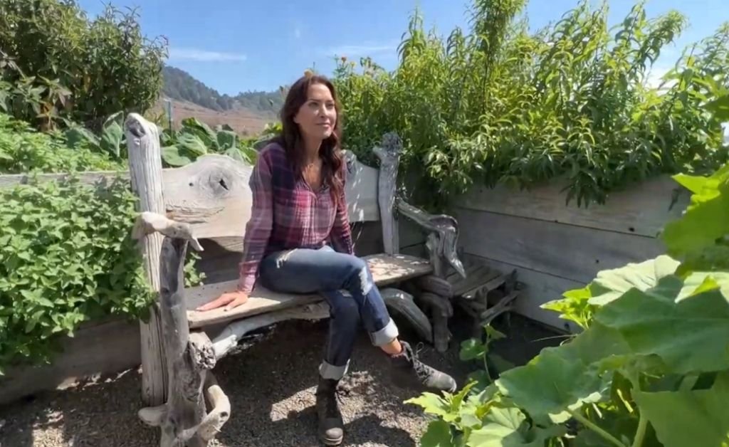 Karen sits on a driftwood bench surrounded by lush garden plants.