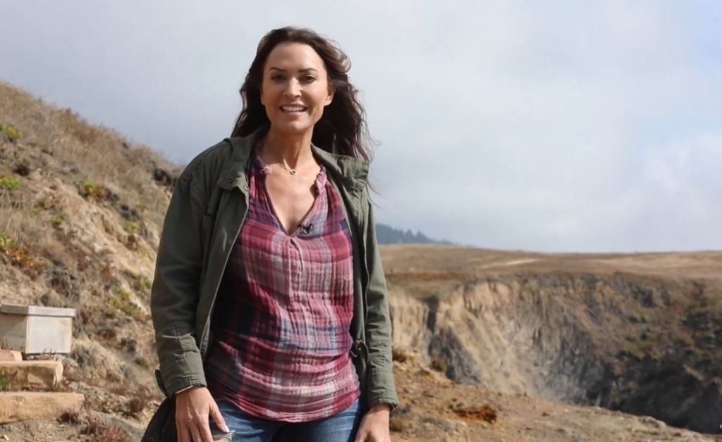 Karen stands on a windswept bluff along the Mendocino Coast, with rugged cliffs and misty hills behind her.