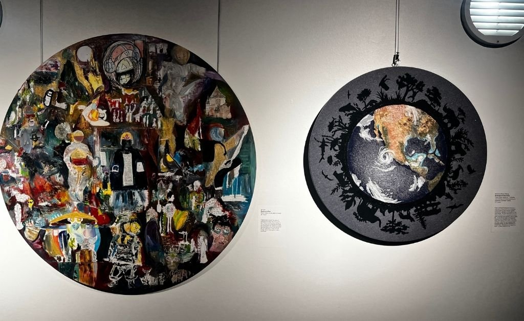 Two circular mixed-media artworks displayed side by side, one featuring layered astronaut and human imagery, the other depicting Earth surrounded by silhouetted figures and animals.