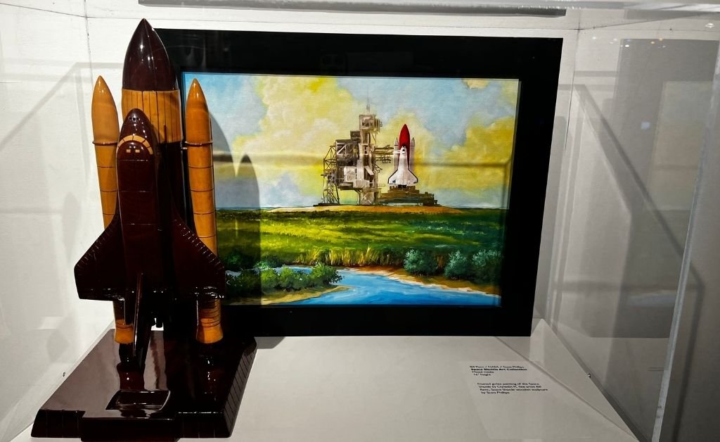 Mixed-media Space Shuttle artwork featuring a framed painting by Bill Renc and a wooden shuttle sculpture by Scott Phillips, displayed at Orlando Science Center.