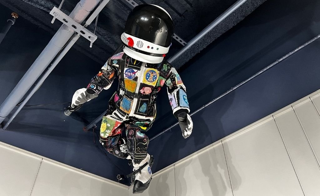 BEYOND Art Spacesuit installation suspended overhead, featuring a patchwork spacesuit decorated with artwork created by children from around the world.